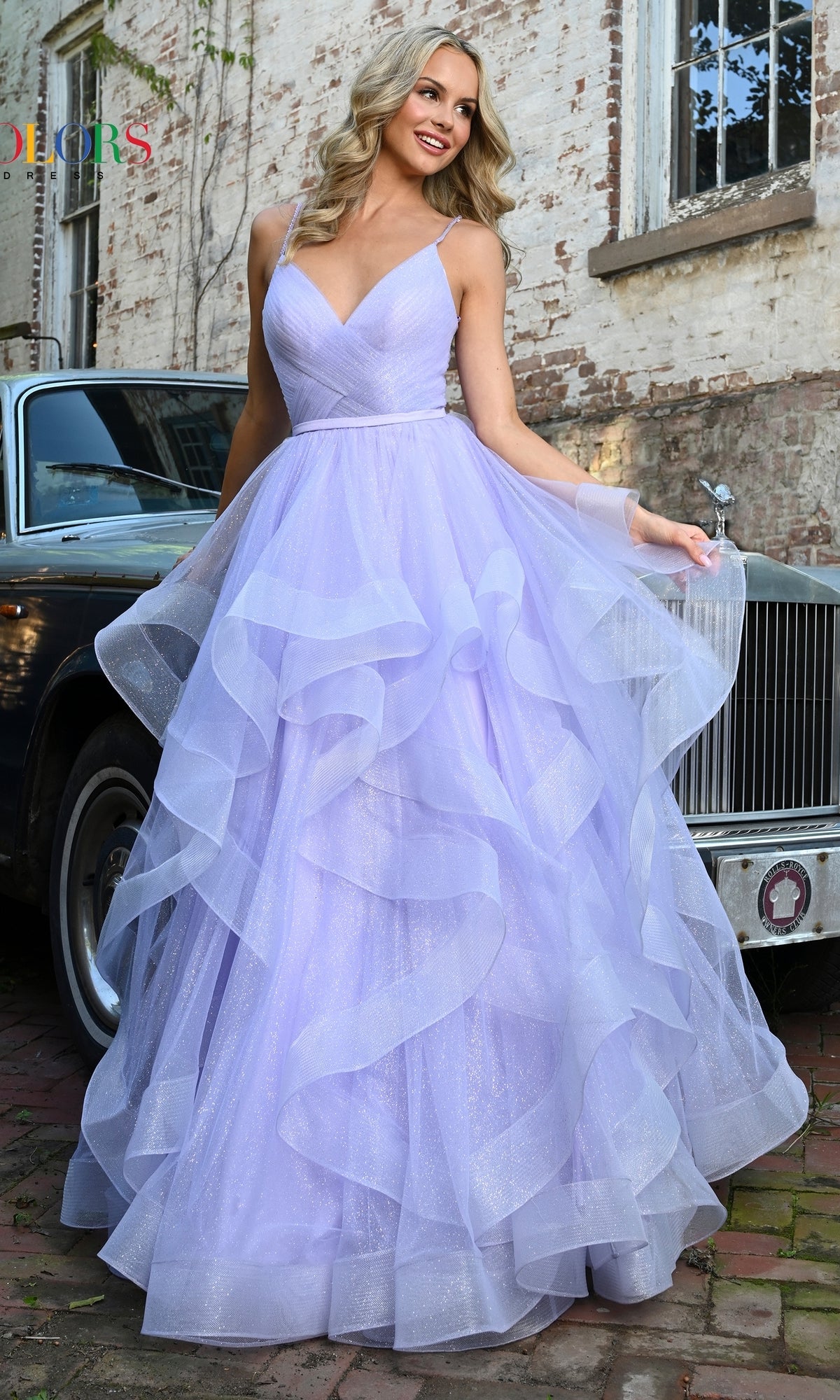 A woman in the Layered Long Tulle Prom Ball Gown 2381, featuring a ruffled a-line tulle skirt, poses outdoors before a vintage car and brick building.